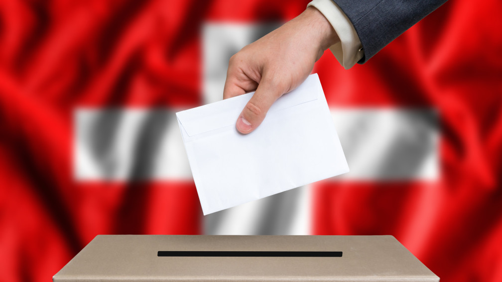 Hand fügt Brief in Urne, Flagge im Hintergrund