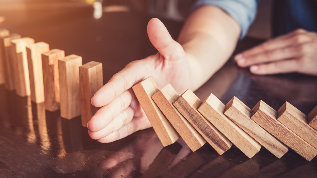 Eine Hand stoppt einen Dominofall