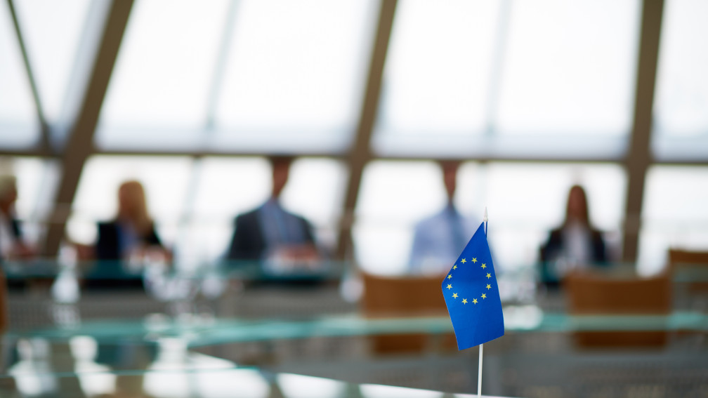 Kleine Europafahne im Fokus im Vordergrund, im Hintergrund Politiker am Tisch