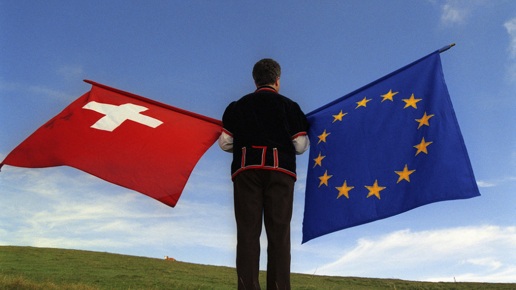 Un homme de dos tient un drapeau suisse et un drapeau européen