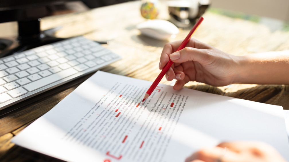 Textdokument und Hand die mit Rotstift Fehler markiert
