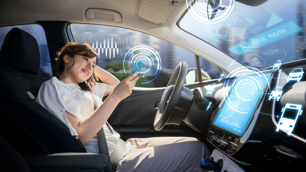 Une jeune femme assise au volant d'une voiture autonome regarde l'écran de son smartphone
