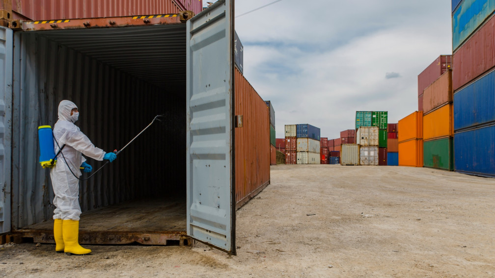 Mann in Schutzanzug desinfiziert einen Gütercontainer