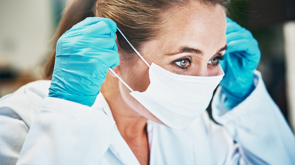 Ärztin mit Schutzhandschuhen zieht Atemschutzmaske an