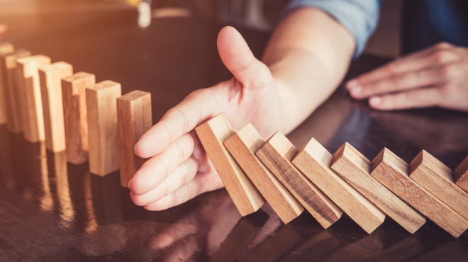 Eine Hand stoppt einen Dominofall