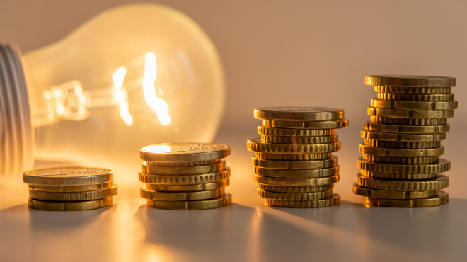 Lampadina accesa dietro a quattro pile di monetine con differenti altezze