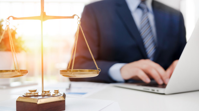 Mann in Anzug vor Laptop, davor Justizwaage