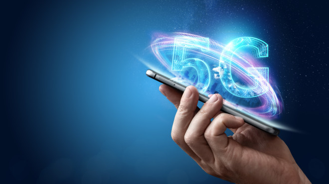 Digitaler Schriftzug "5g" fliegt über Handy das von einer Hand gehalten wird