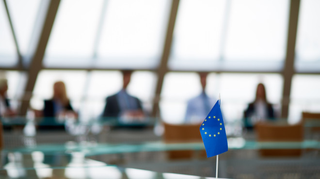 Kleine Europafahne im Fokus im Vordergrund, im Hintergrund Politiker am Tisch