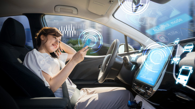 Une jeune femme assise au volant d'une voiture autonome regarde l'écran de son smartphone
