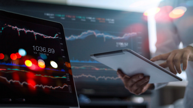 2 Computerbildschirme mit Statistiken darauf und eine Hand mit IPad ein Finger zeigt darauf