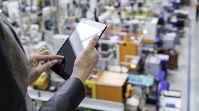 Frau mit Tablet, im Hintergrund eine Fabrik