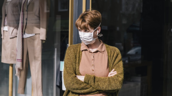 Frau mit Maske steht vor ihrem geschlossenen Kleidergeschäft