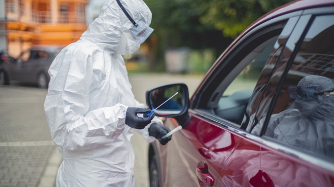 Person in Schutzanzug testet Fahrer eines Autos auf Corona