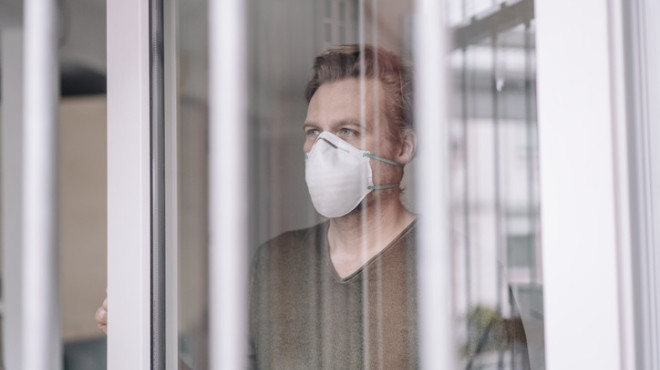 Mann mit Atemmaske steht hinter Fenster