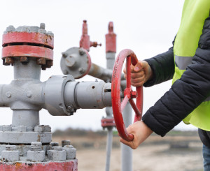 mani di persona con pettorina di sicurezza con catarifrangenti gira la ruota di rubinetto del gas