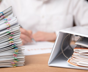 Grosser Stapel Akten, arbeitender Mann im Hintergrund 