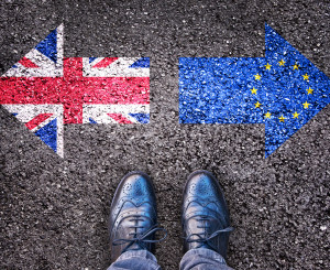 Zwei Füsse stehen vor zwei Pfeilen. Nach links zeigt der Pfeil mit Grossbritanniens Flagge, nach rechts der Pfeil mit der EU Flagge