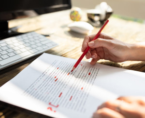 Textdokument und Hand die mit Rotstift Fehler markiert