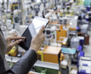 Frau mit Tablet, im Hintergrund eine Fabrik