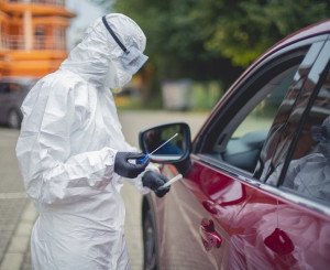 Person in Schutzanzug testet Fahrer eines Autos auf Corona