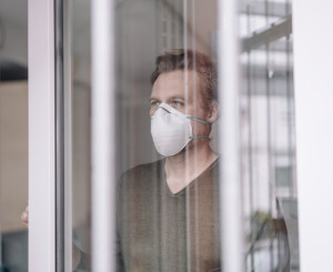 Mann mit Atemmaske steht hinter Fenster