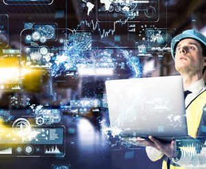 Mann in einem Industriebetrieb mit Laptop und digitaler Projektion vor sich